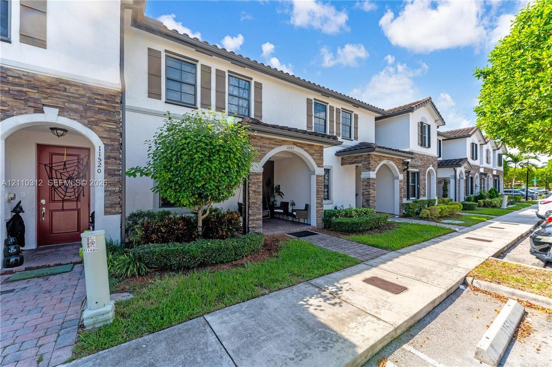 Mediterranean-style exterior featuring smooth stucco facade, decorative stone veneer, arched entryway, brick-paver walkway, and dark-frame windows