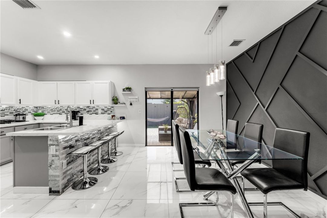 Kitchen featuring white cabinetry, stone-finish countertops, a multi-textured stone backsplash, glossy tile flooring, and an accent wall with geometric millwork