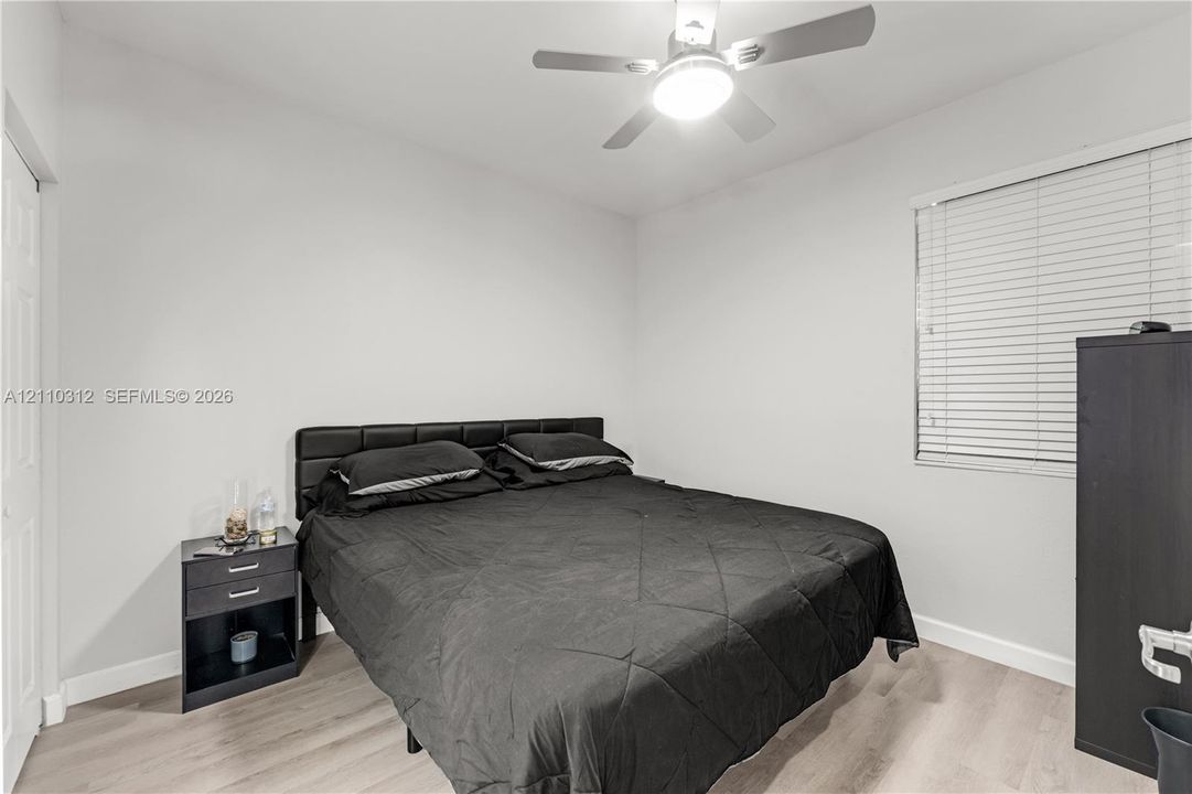 Interior room featuring wood-finish flooring, white walls, horizontal window blinds, and a ceiling fan with integrated light fixture