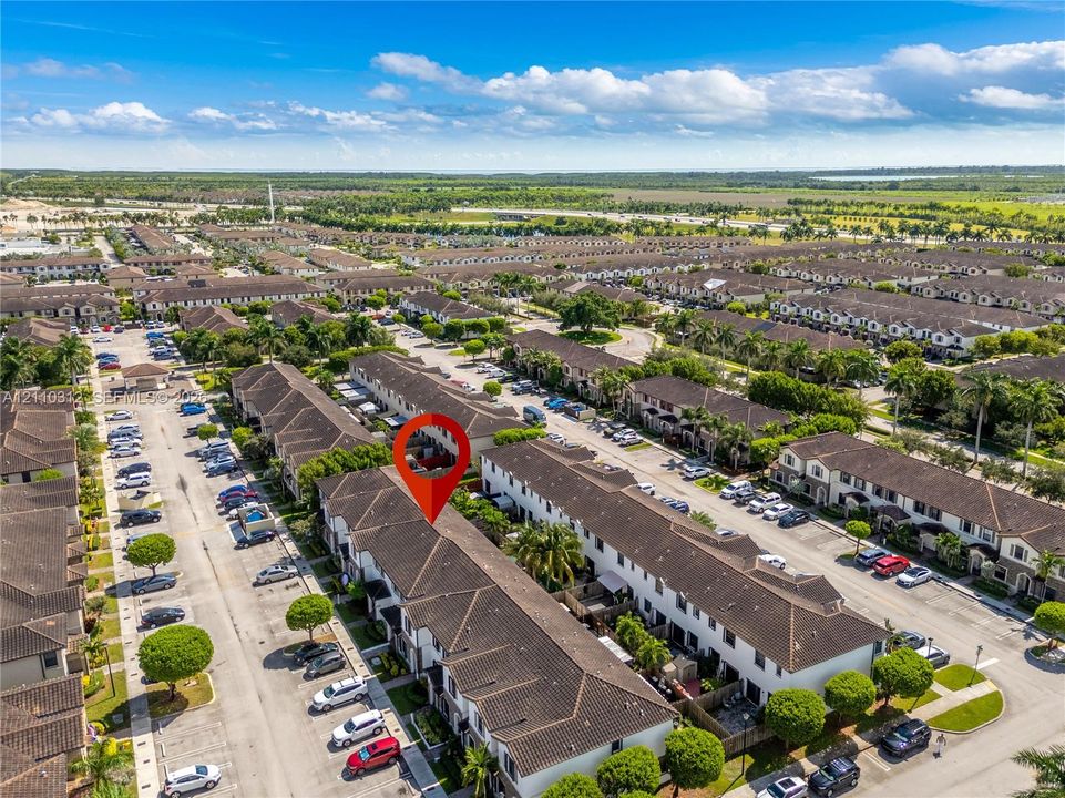 Aerial perspective of a multi-unit residential development featuring a tile roof, paved parking areas, and mature landscaping