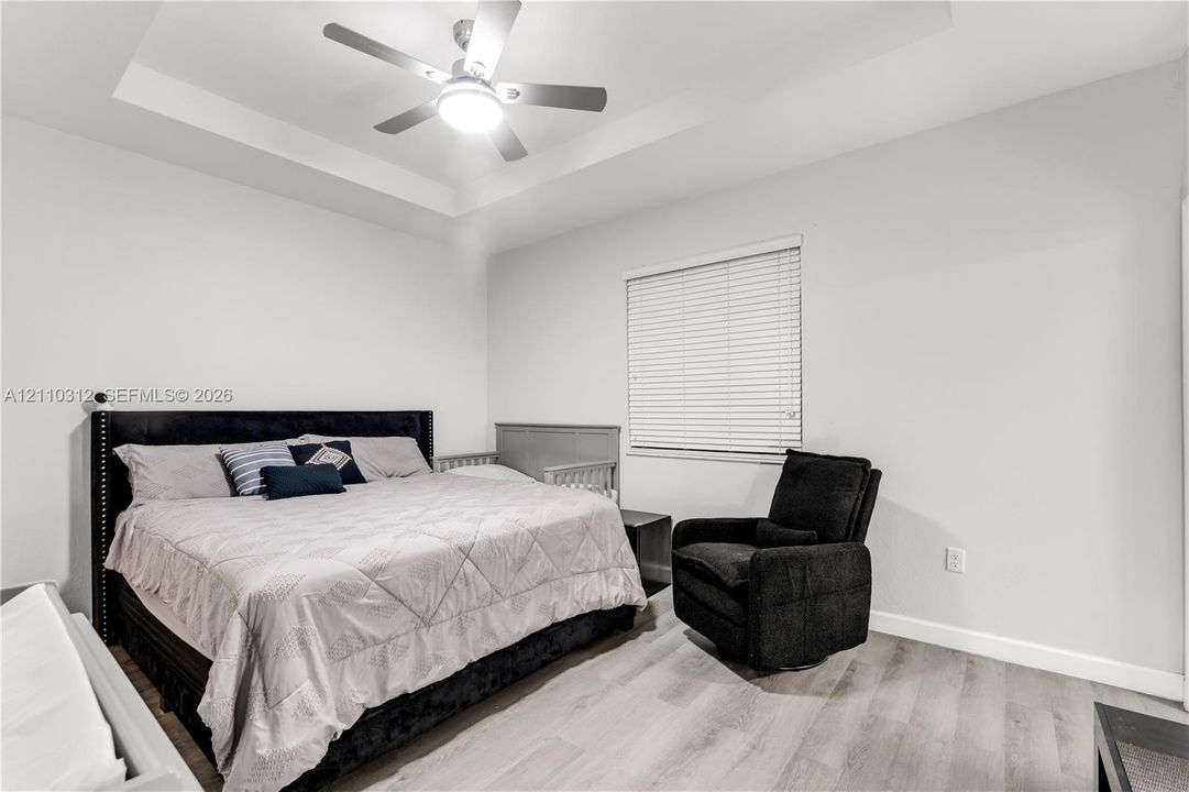 Tray ceiling, multi-speed ceiling fan with integrated light fixture, wood-finish flooring, and horizontal window blinds
