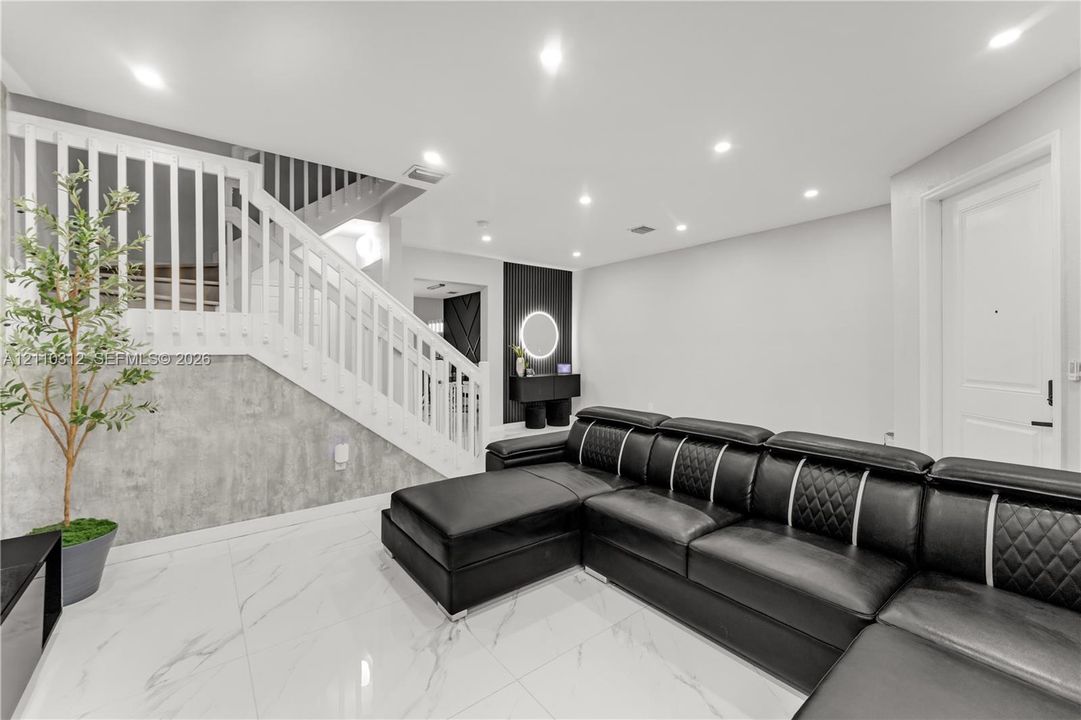 Polished tile flooring, recessed lighting, white wood-slat staircase railing, gray stone-finish wall paneling, and a circular LED wall fixture
