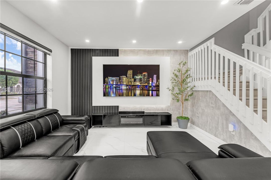 Living area featuring large-format tile flooring, recessed lighting, and a focal wall with vertical slat paneling and integrated entertainment cabinetry
