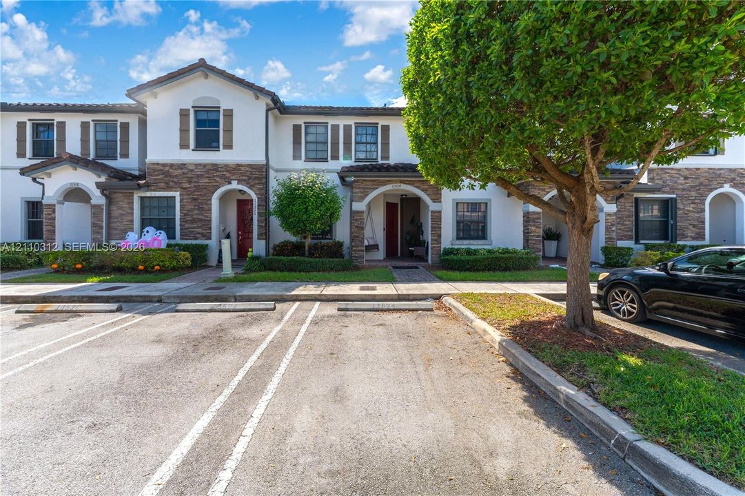 Multi-unit exterior featuring stucco and stone-veneer siding, arched entryway detailing, tile roofing, and assigned parking spaces