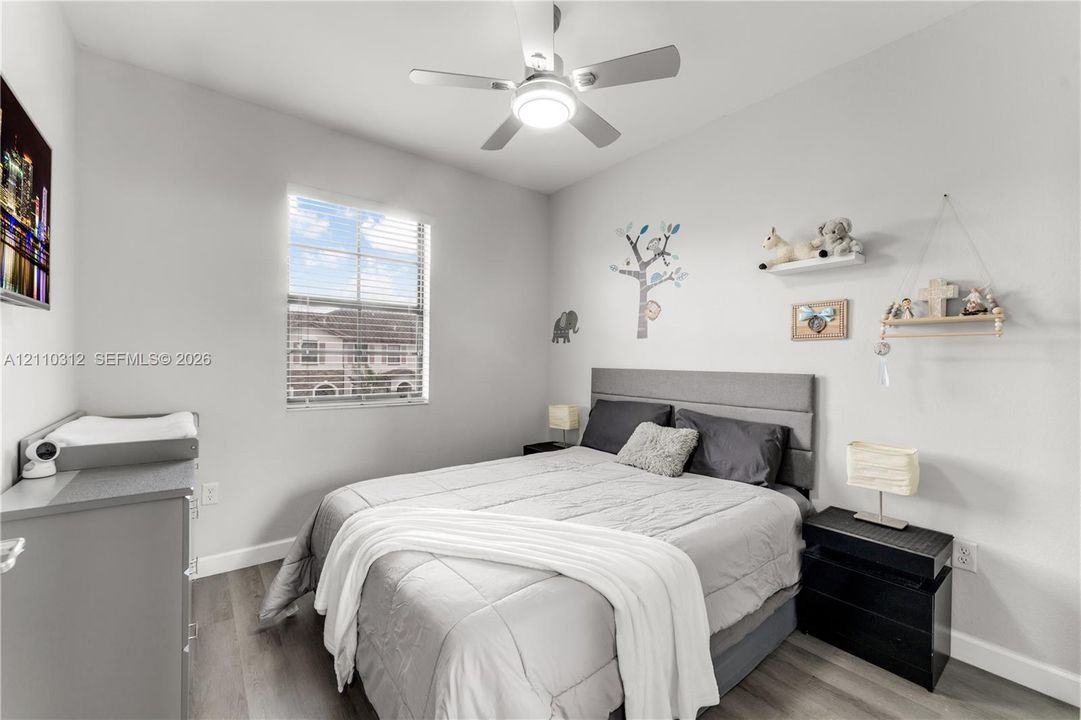 Bedroom featuring wood-finish flooring, a neutral color palette, a single-pane window with horizontal blinds, and a ceiling-mounted light fixture with an integrated fan