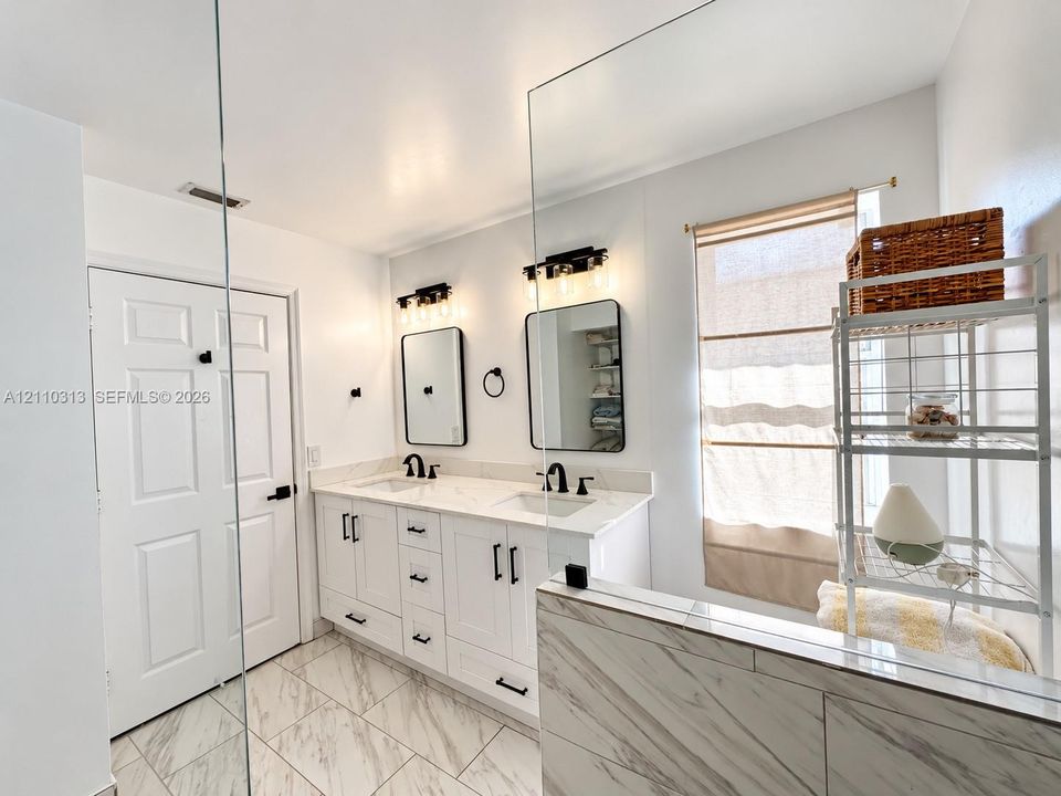 Dual-sink vanity with white cabinetry, light-toned stone-finish countertops, rectangular undermount sinks, matte black fixtures, and framed mirrors
