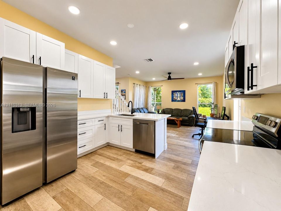 Kitchen featuring white cabinetry with dark hardware, stone-finish countertops, stainless steel appliances, and wood-finish flooring
