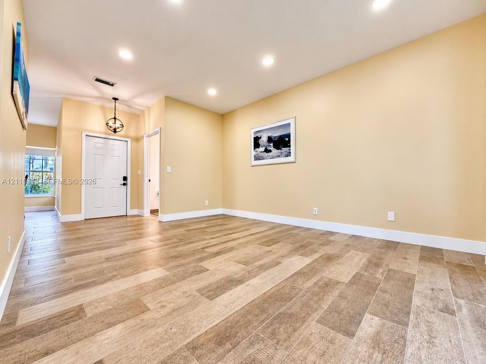 Open interior space featuring wood-finish tile flooring, recessed ceiling lighting, and a six-panel entry door with a metal lantern-style pendant fixture
