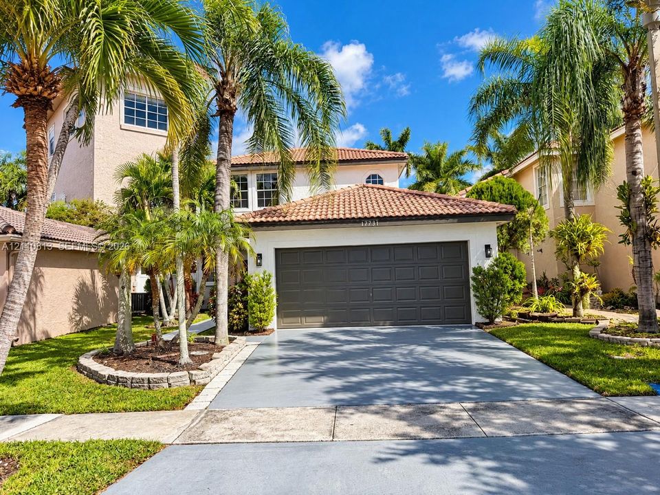 Two-story exterior featuring a tile roof, neutral stucco finish, paneled garage door, concrete driveway, and established palm landscaping with stone edging