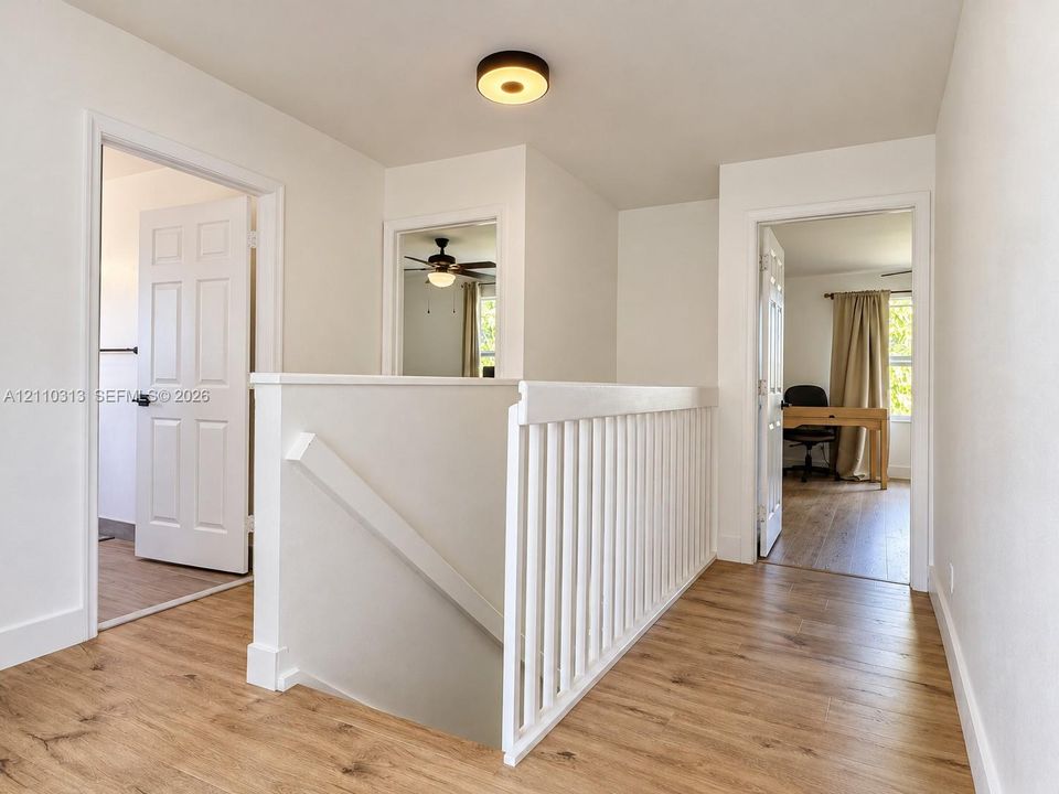 Hallway featuring wood-finish flooring, a white wooden balustrade, and a flush-mount circular ceiling light fixture