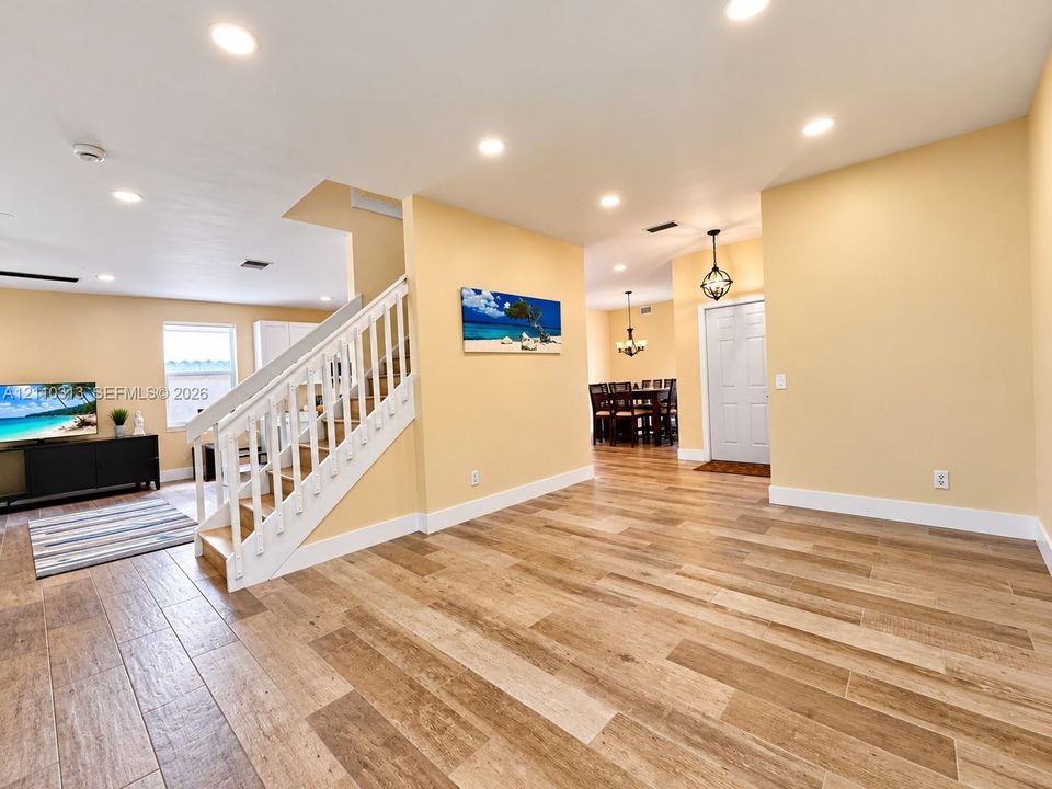 Open-concept interior featuring wood-finish tile flooring, recessed ceiling lighting, and a staircase with a white balustrade