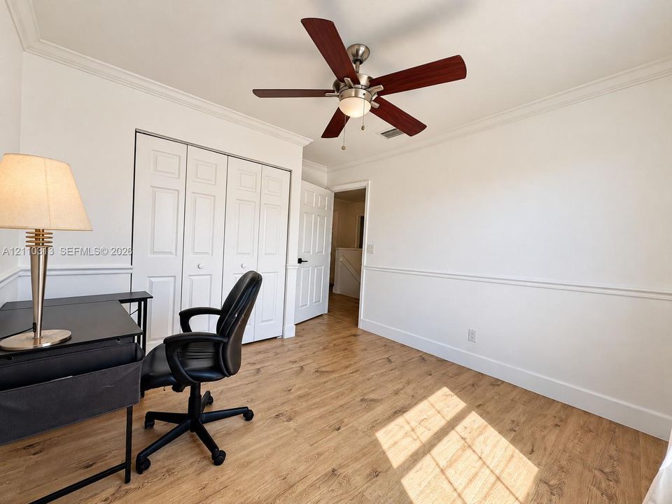 Room featuring wood-finish flooring, crown molding, chair rail molding, a multi-panel closet door, and a ceiling fan with integrated lighting