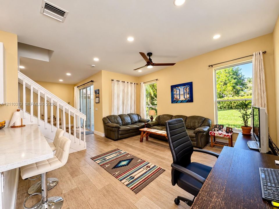 Open-concept interior featuring wood-finish flooring, recessed lighting, a ceiling fan, sliding glass doors, and a breakfast bar with a stone-finish countertop