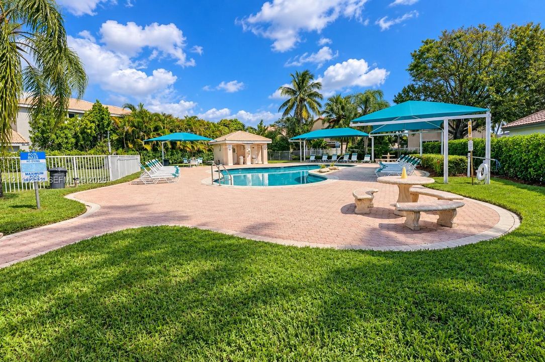 Community pool featuring a paved deck, permanent shaded structures, built-in masonry seating, and manicured landscaping