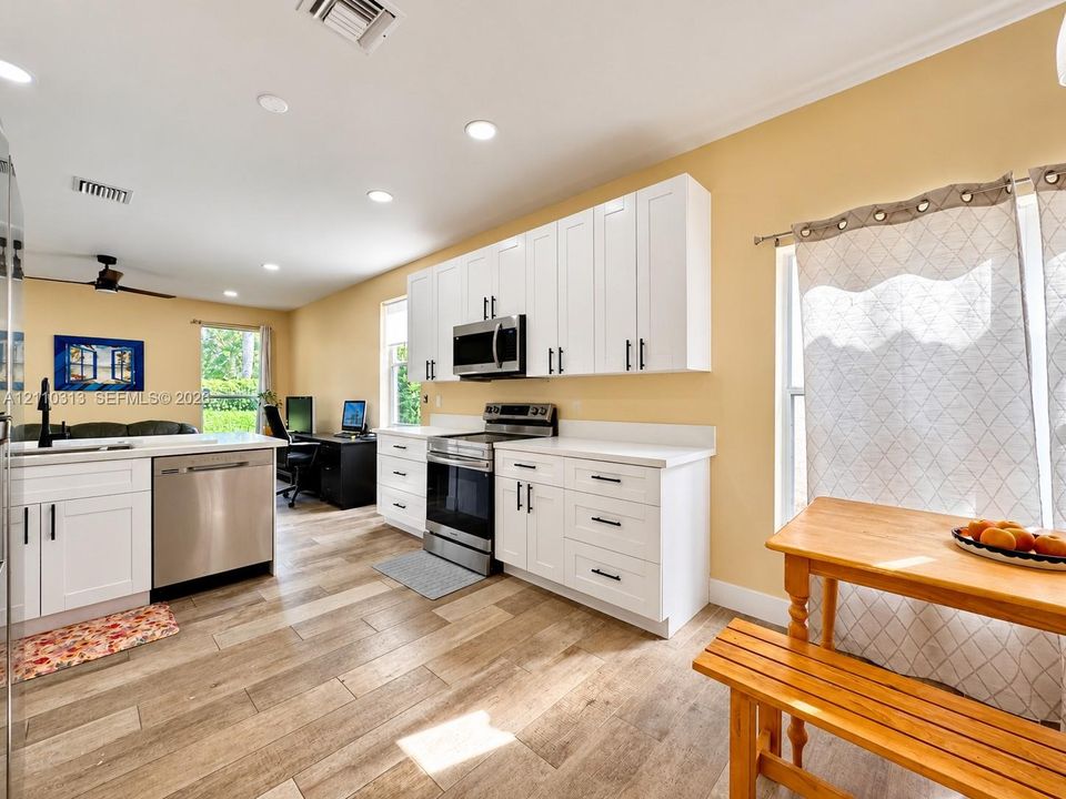 Kitchen featuring white Shaker-style cabinetry, stainless steel appliances, solid-surface countertops, and wood-finish flooring
