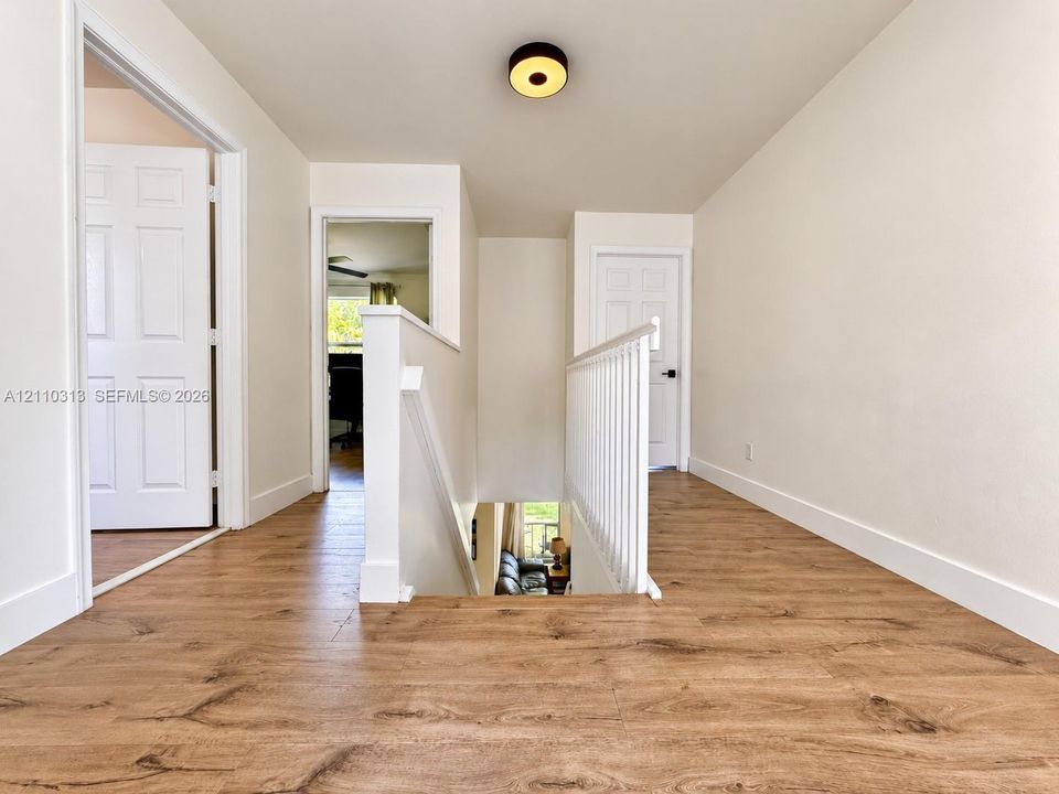 Landing area featuring wood-finish flooring, white paneled interior doors, a white wooden staircase railing, and a circular flush-mount ceiling light fixture