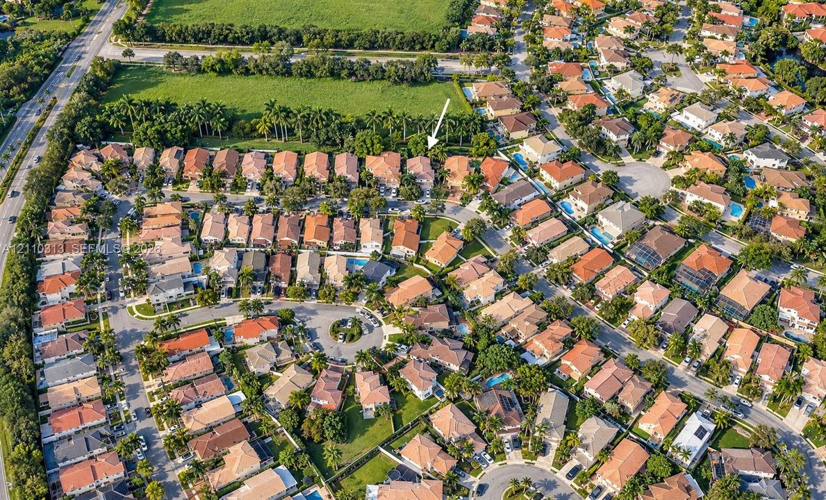Aerial perspective of a residential community featuring tile-roofed architecture, paved street grids, landscaped green spaces, and dense perimeter foliage