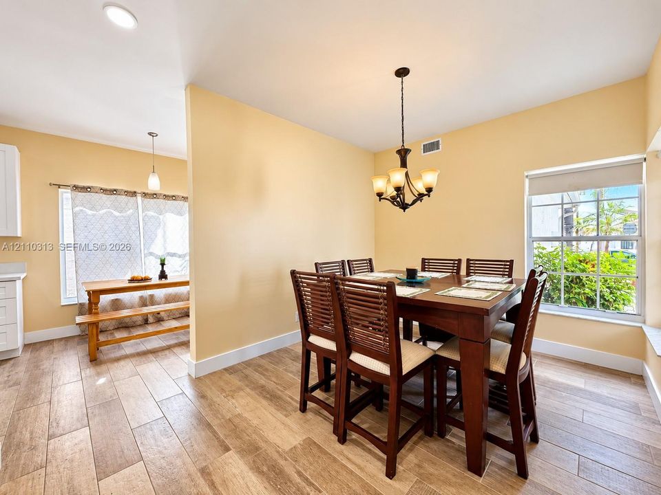 Wood-finish tile flooring, multi-light chandelier, recessed lighting, and large windows providing natural illumination