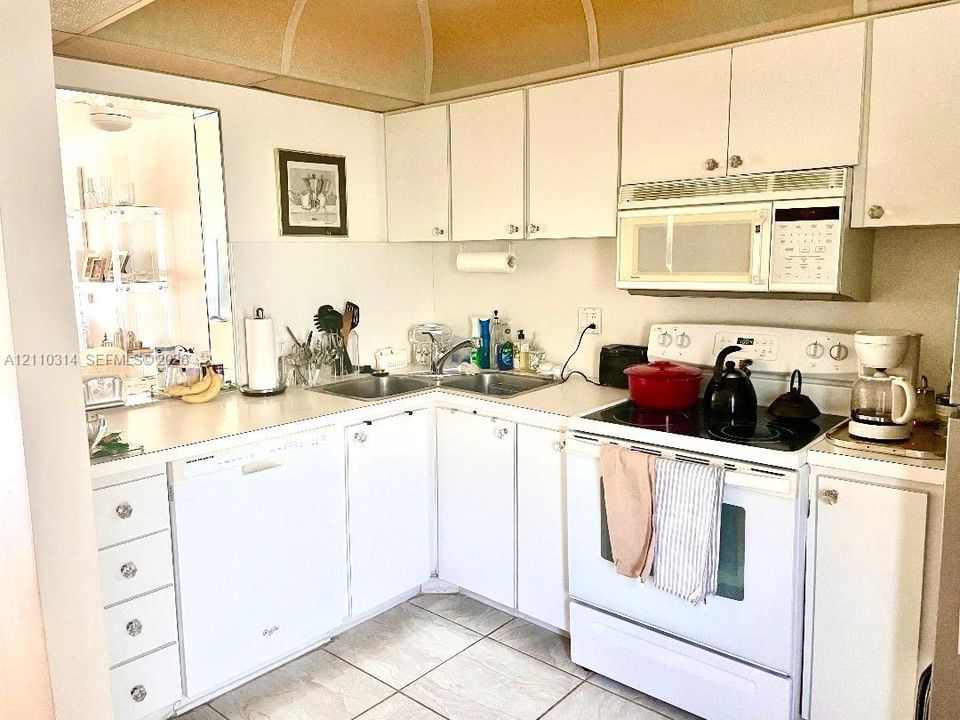 Kitchen featuring flat-panel cabinetry, a stainless steel double-basin sink, a built-in over-the-range microwave, a four-burner electric range, and ceramic tile flooring