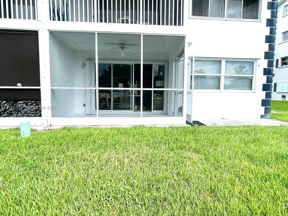 Screened-in patio featuring a ceiling fan and sliding glass doors, exterior siding, and a grass lawn