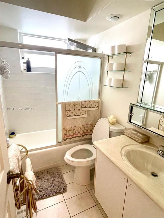 Full bathroom featuring tile flooring, a built-in vanity with integrated basin, glass-shelving unit, and a bathtub with etched-glass sliding doors