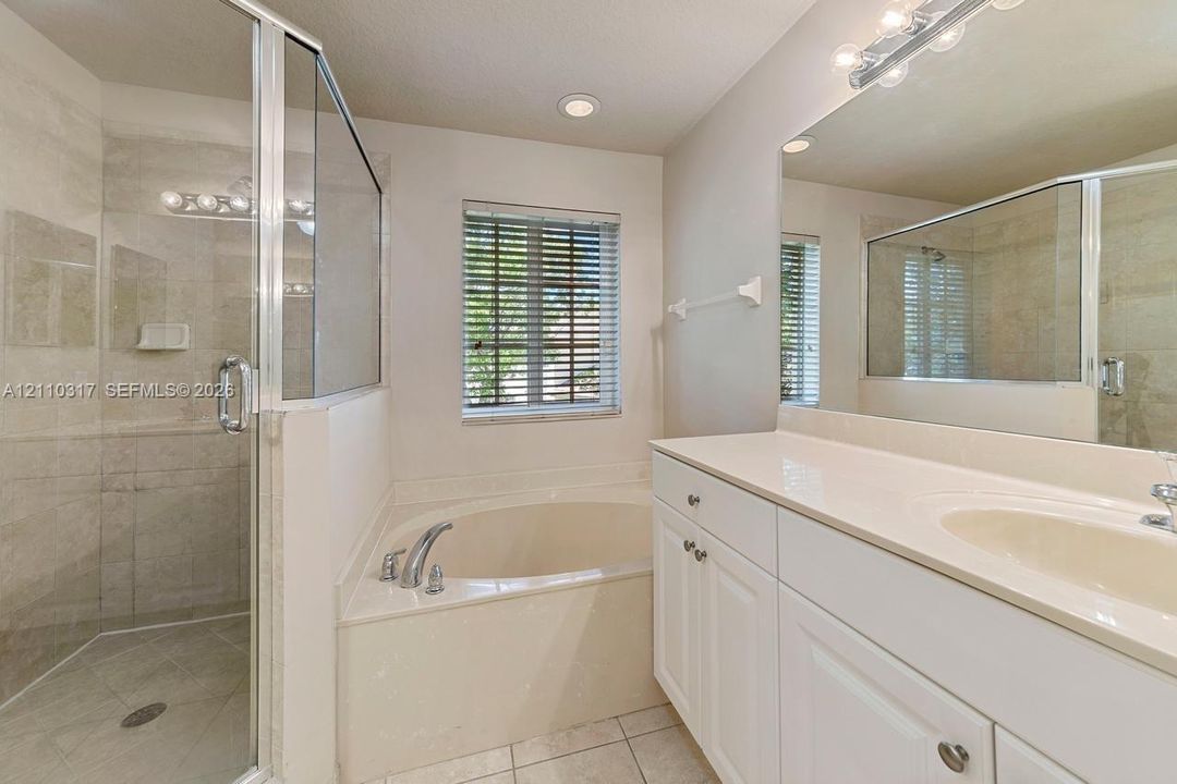 Bathroom featuring a separate glass-enclosed shower, soaking tub, vanity with a solid-surface countertop, and a large wall-mounted mirror