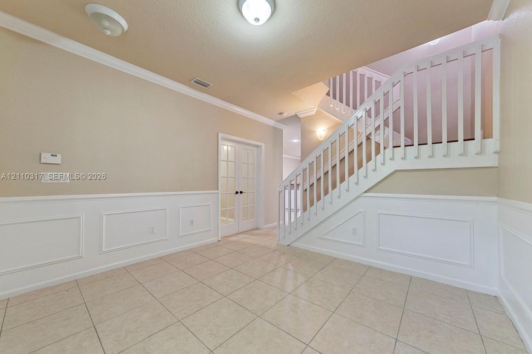 Foyer featuring neutral tile flooring, white wainscoting, a staircase with white balusters, and French doors with glass panes