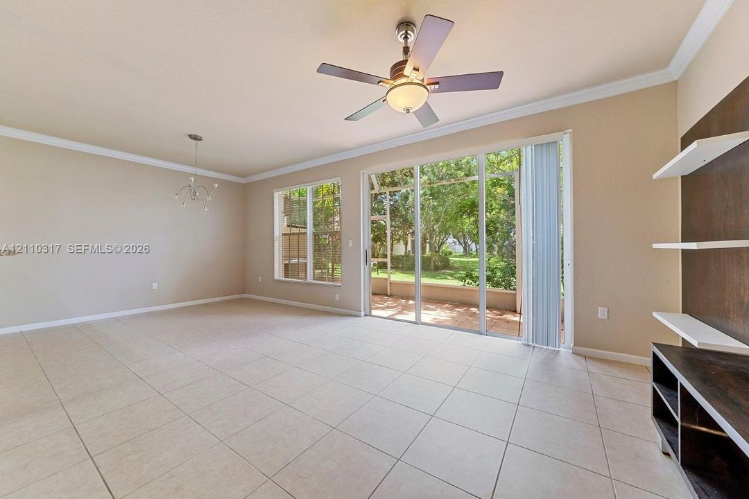 Living area featuring large format tile flooring, a multi-blade ceiling fan with integrated lighting, crown molding, built-in shelving, and sliding glass doors