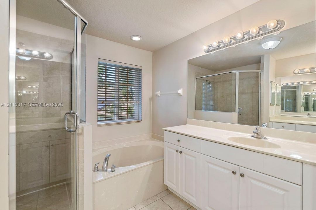 Bathroom featuring a glass-enclosed shower, a deep soaking tub, white cabinetry, a large wall-mounted mirror, and tile flooring