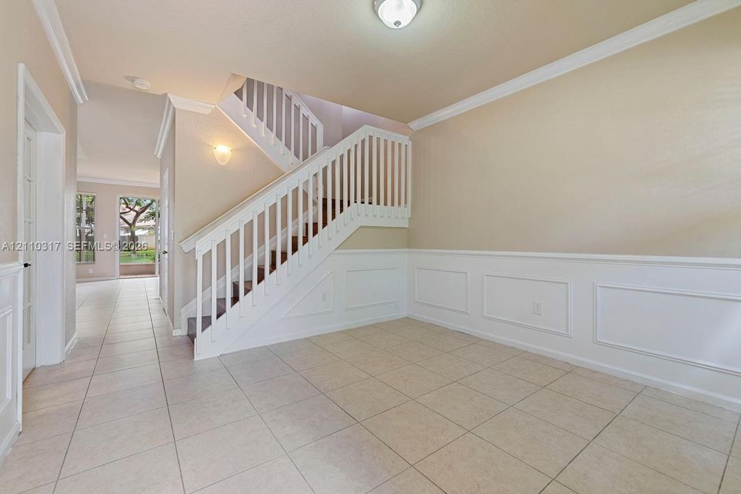 Ceramic tile flooring, staircase with white wooden balustrades, crown molding, and decorative wall wainscoting