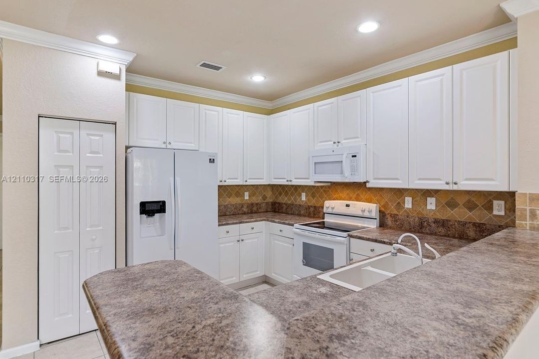 Kitchen featuring white cabinetry, solid-surface countertops, dual-basin sink, tiled backsplash, and recessed lighting