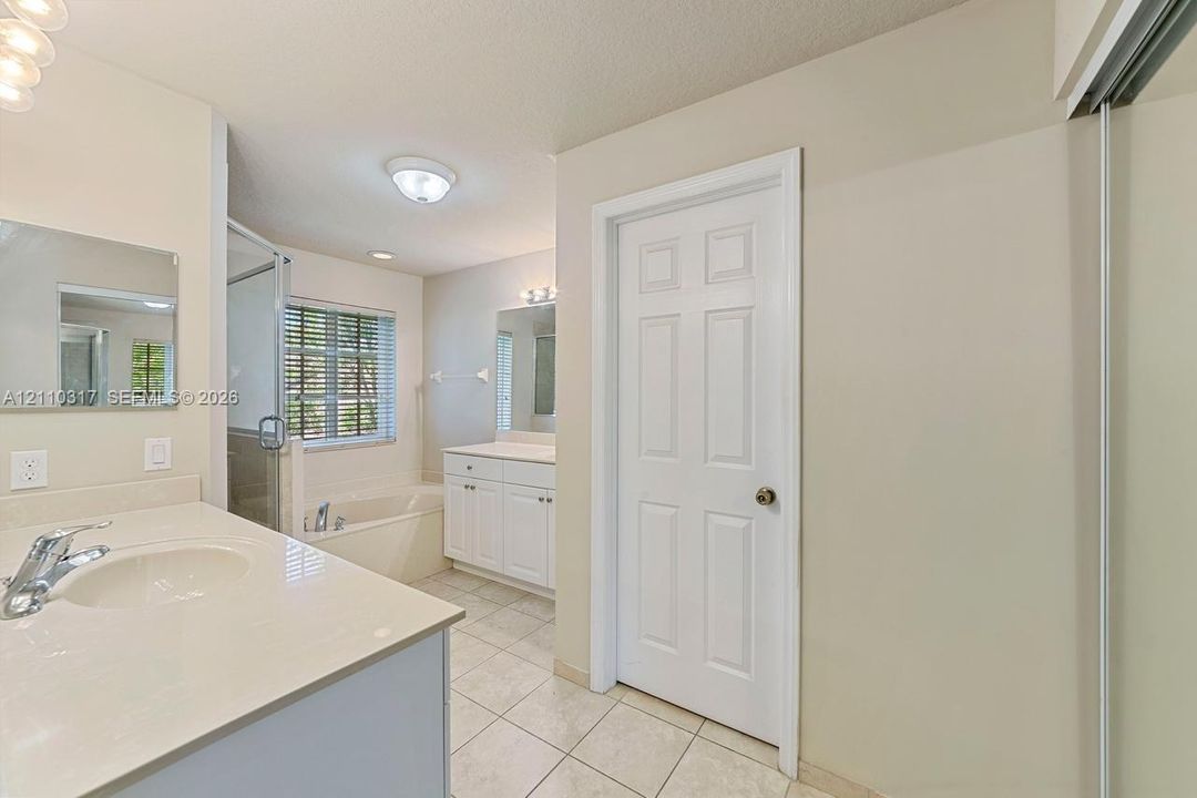 Bathroom featuring white cabinetry, solid-surface vanity countertops with integrated sinks, ceramic tile flooring, and a glass-enclosed shower and tub combination