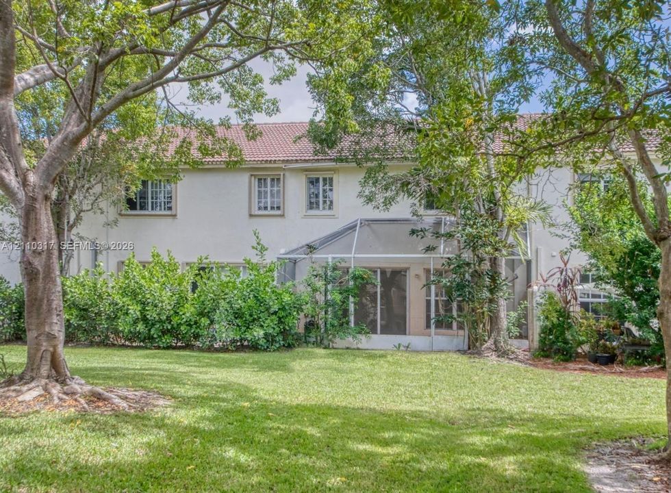 Two-story stucco exterior with a tile roof, featuring a screened-in lanai, multi-pane windows, and a landscaped backyard with mature trees