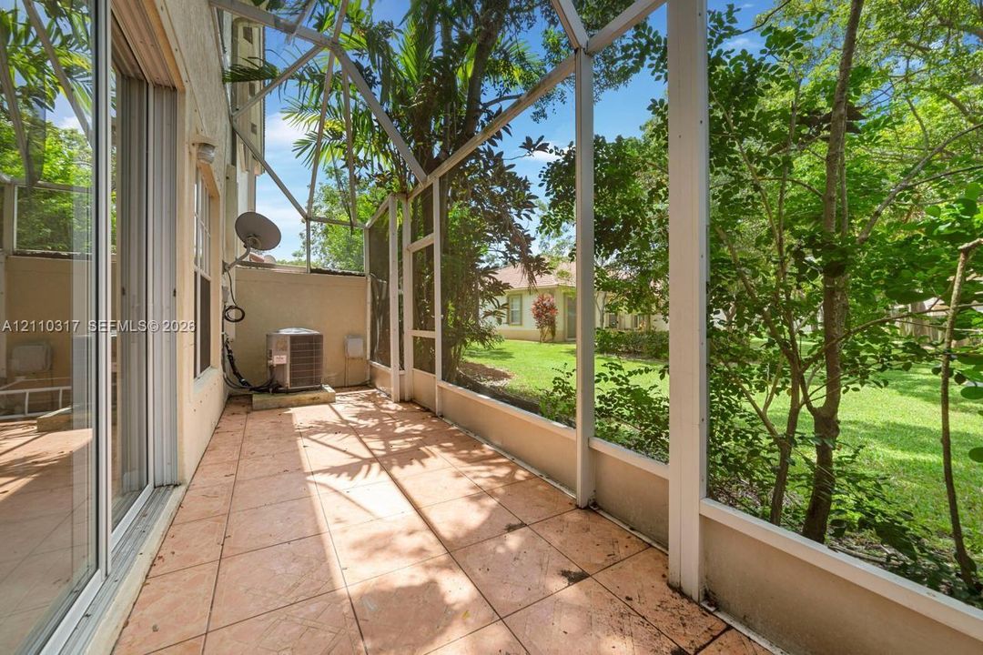 Screen-enclosed patio featuring tile flooring, sliding glass door entry, and mature landscaping