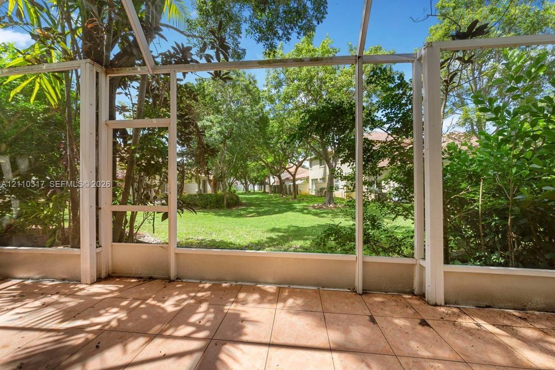Screened-in patio with tiled flooring and metal frame construction overlooking a grass lawn with mature trees