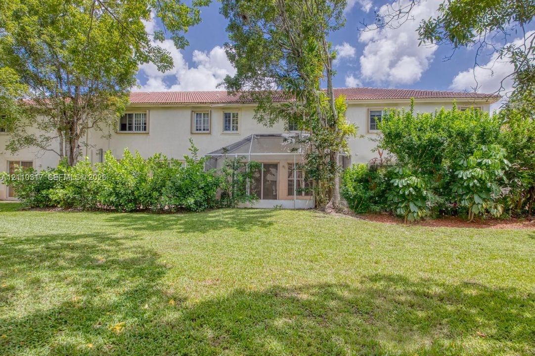 Two-story stucco exterior featuring a tile roof, an enclosed screened lanai, and landscaped grounds with mature trees
