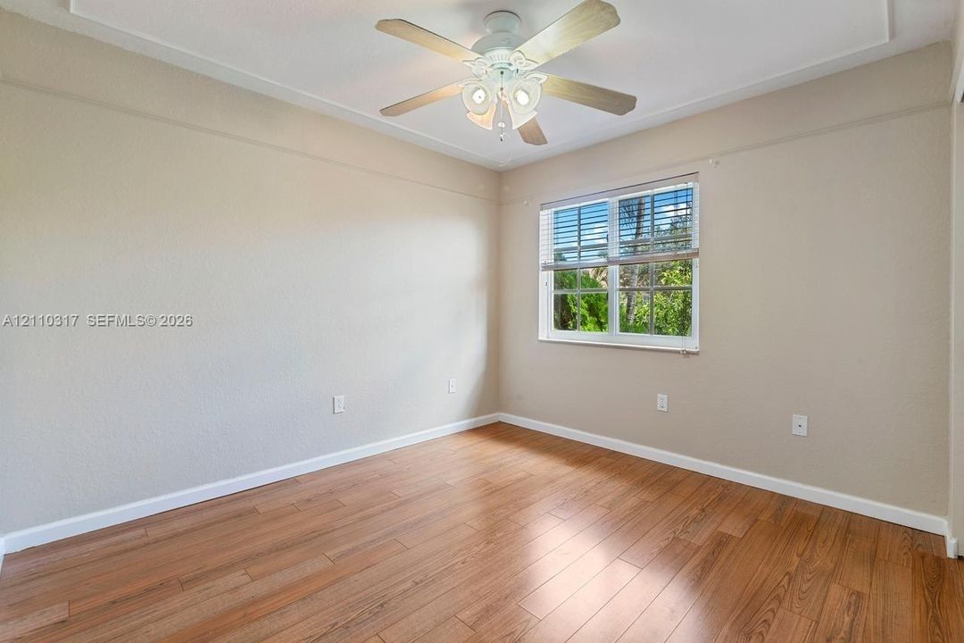 Room featuring wood-finish flooring, a multi-blade ceiling fan with integrated lighting, and a window with white frame trim