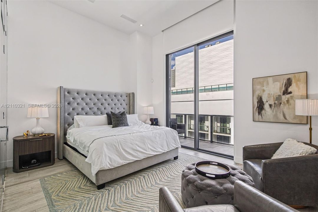 High-ceilinged room with full-height windows, floor-to-ceiling sliding glass door, and wood-finish flooring