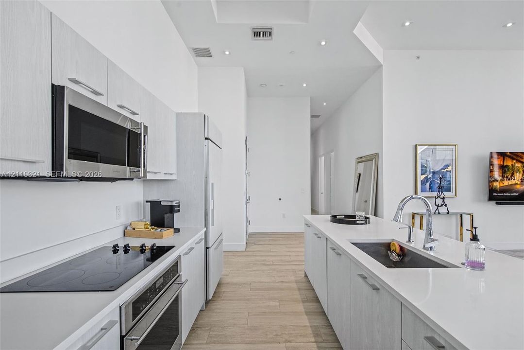 Modern kitchen featuring light-toned cabinetry, stainless steel appliances, a center island with an undermount sink, quartz countertops, and wood-finish flooring