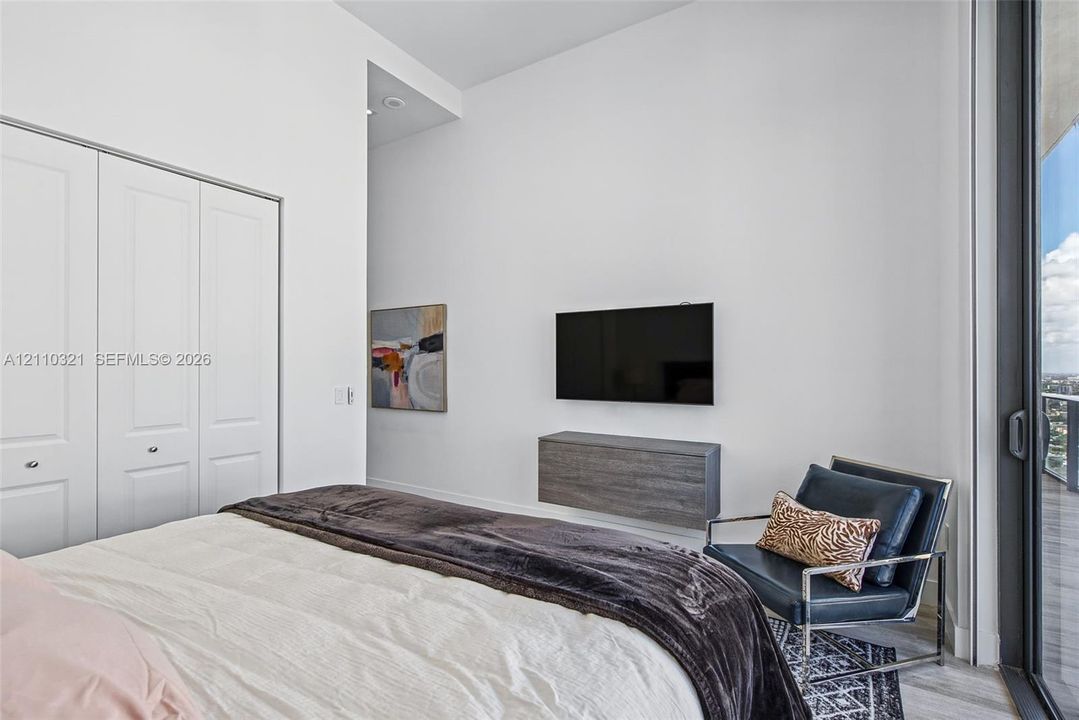 High-ceiling room featuring a wall-mounted floating storage unit, full-height double-door closet with paneled detailing, and a floor-to-ceiling glass sliding door