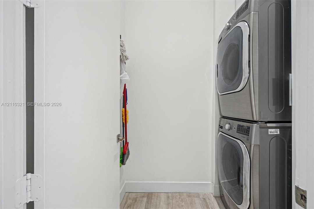 Stacked stainless steel laundry appliances with wood-finish flooring