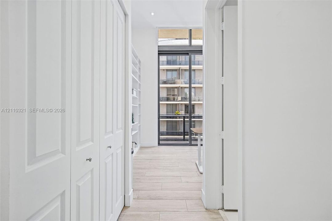 Floor-to-ceiling built-in shelving, wood-finish flooring, sliding glass balcony door, recessed ceiling lighting, and paneled closet doors