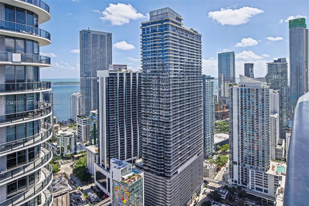 High-rise urban landscape featuring floor-to-ceiling glass facades, wrap-around balconies, expansive water horizons, and dense metropolitan infrastructure
