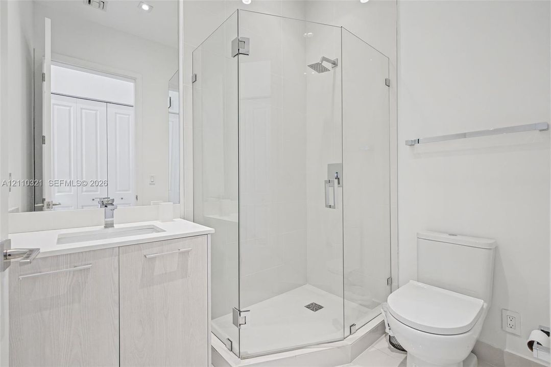 Bathroom featuring a wood-finish vanity with a rectangular sink, quartz countertop, chrome faucet, glass-enclosed shower, and a two-piece toilet
