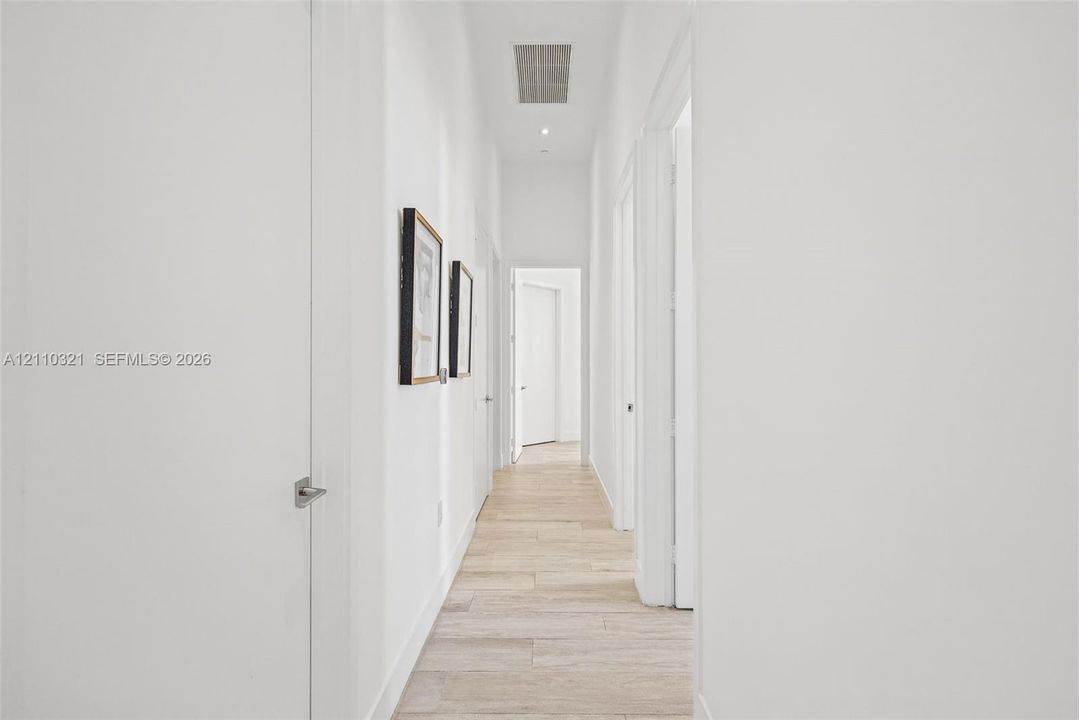 Hallway featuring light-toned wood-finish flooring, crisp white wall finishes, and multiple interior swing doors with satin nickel hardware