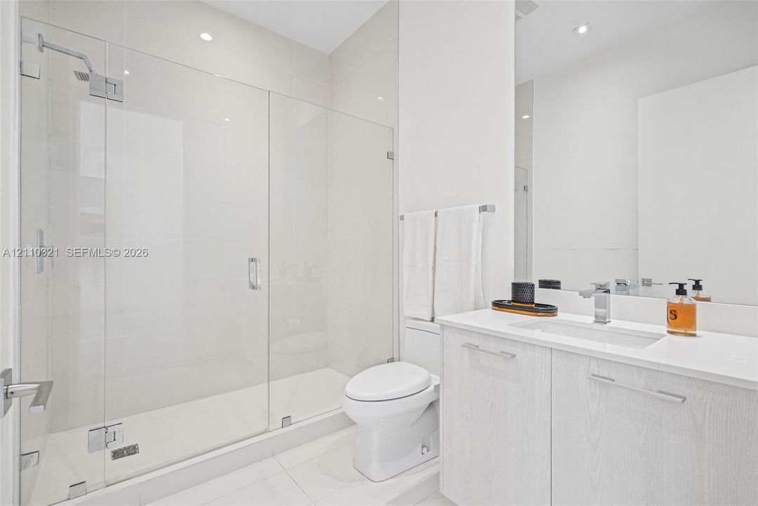 Bathroom featuring a glass-enclosed walk-in shower with chrome fixtures, wood-finish vanity cabinetry, a rectangular undermount sink, and a quartz countertop