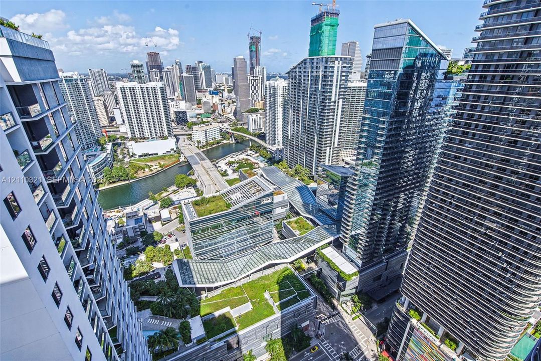High-rise cityscape perspective featuring extensive glass-facade towers, urban waterway, multi-level architectural structures with green roofing, and dense metropolitan density