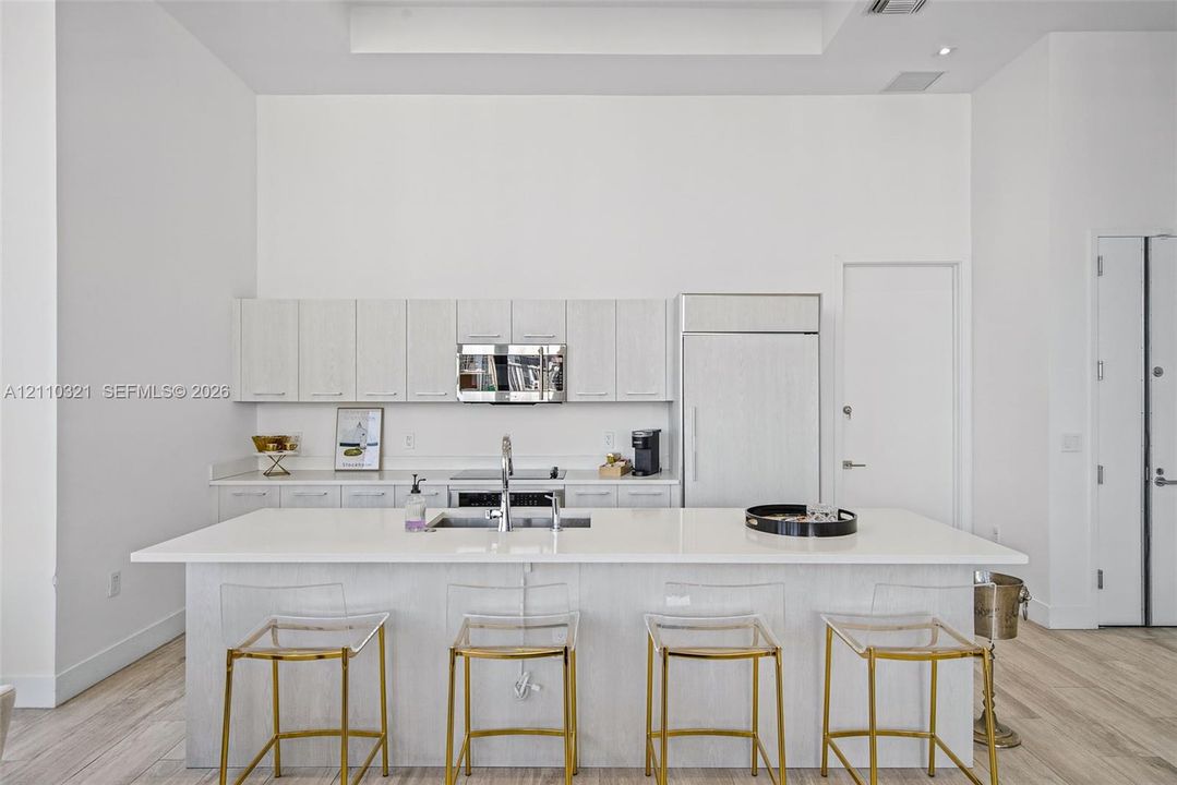 Kitchen featuring light wood-finish cabinetry, a large central island with solid surface countertops, stainless steel appliances, and wood-finish flooring