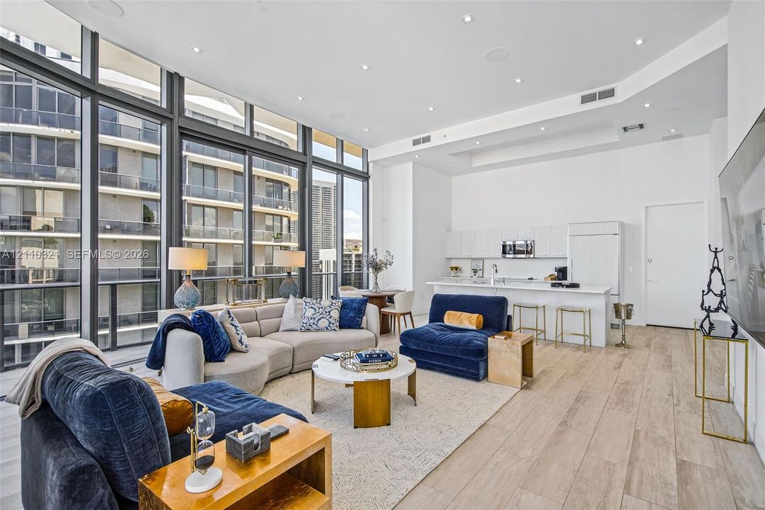 Floor-to-ceiling windows, open-concept kitchen with white cabinetry, built-in breakfast bar, and wood-finish flooring