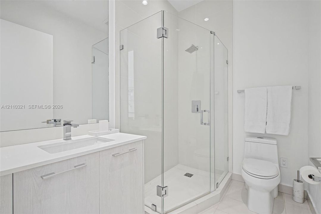 Bathroom featuring a wood-finish vanity with a rectangular undermount sink, stone-surface countertop, walk-in glass-enclosed shower with polished chrome fixtures, and a dual-flush toilet